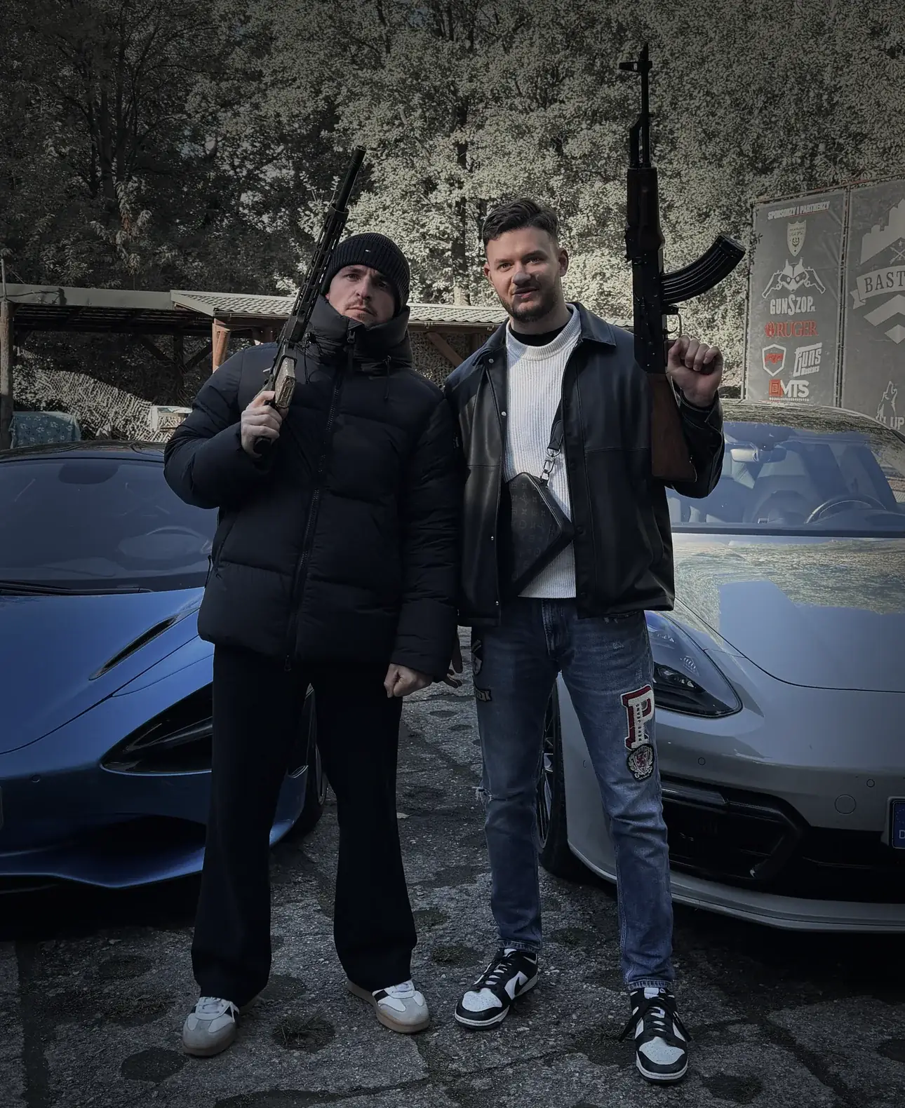 Zwei Männer mit Gewehren am Schießstand vor einem McLaren und einem Porsche